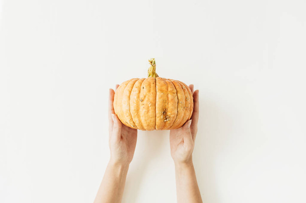 weibliche Hand mit gelbem Kürbis auf weißem Hintergrund. Herbst-Halloween-Konzept. flache Lage, Draufsicht. - Foto, Bild