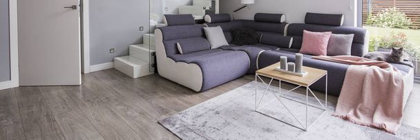 Real photo of grey Scandinavian style living room interior with corner couch with blanket and pillows and end table with candles placed on carpet - Fotó, kép