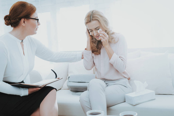 An adult woman at a psychologist's reception. She cries. A female psychologist tries to calm her down. They are sitting on the sofa in the office. - Foto, immagini