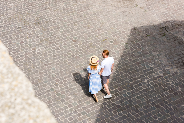 vista de ángulo alto de la pareja pelirroja cogida de la mano y caminando en la calle de la ciudad
 - Foto, Imagen