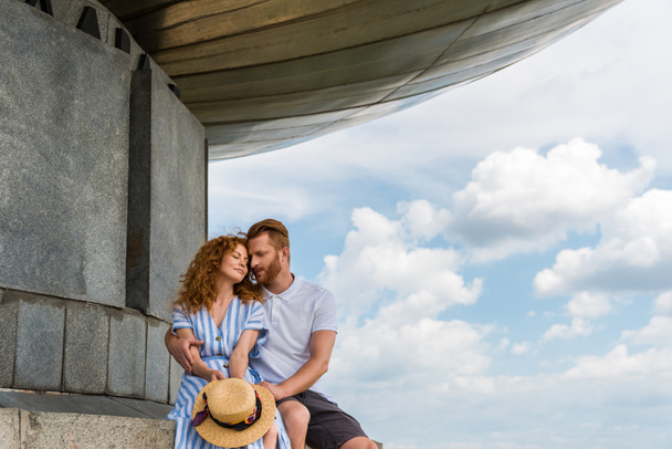 redhead couple sitting near building against blue cloudy sky - Photo, Image