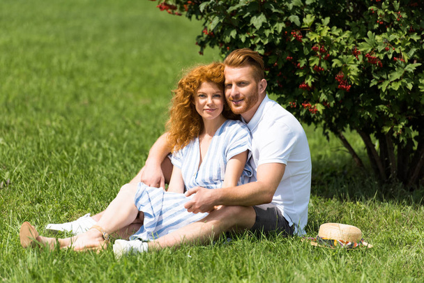 рыжая пара смотрит в камеру и сидит на траве в парке
  - Фото, изображение