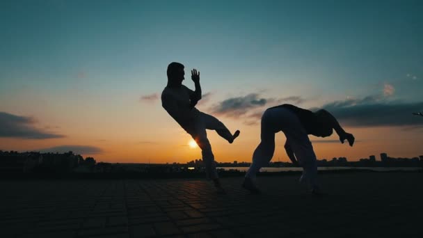 Siluetas de dos hombres deportivos que entrenan habilidades de arte marcial de la capoeira en el fondo del cielo increíble
 - Metraje, vídeo