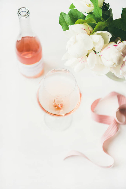 Rose wine in glass and bottle, pink decorative ribbon, peony flowers over white background - Zdjęcie, obraz