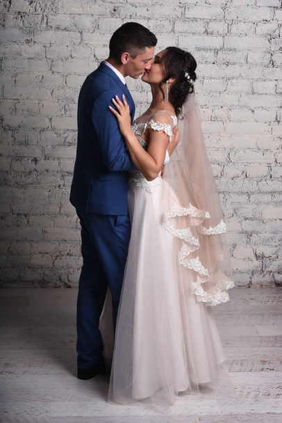 Full length view of newlyweds kissing in studio on brick wall background - Foto, Bild