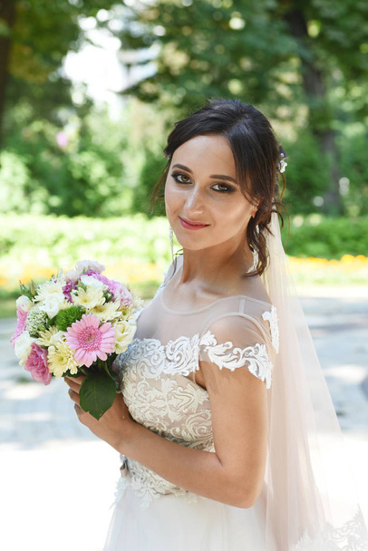junge brünette Braut mit Strauß posiert im Park - Foto, Bild