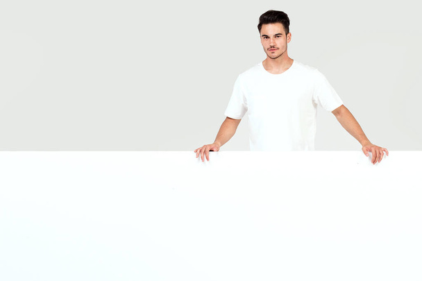 Young handsome guy holding blank white banner, signboard, isolated on white studio background. - Photo, Image