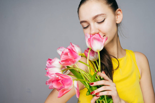 lovely charming girl in a yellow dress smells fragrant pink flowers, enjoys - Fotó, kép