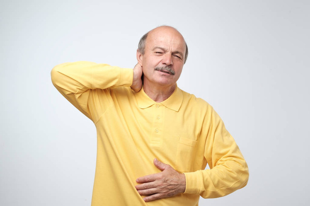 Großaufnahme eines reifen Mannes im gelben T-Shirt mit geschlossenen Augen, der vor Schmerzen seinen Hals berührt. Gesundheitsprobleme im Alter, Neuralgie-Konzept - Foto, Bild