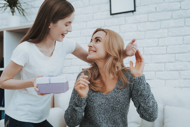 Smiling Daughter Gives Mother Gift in Small Box. Relationship in Family. Holiday at Home. Happy Mother. Friendly Relations. Celebrating Together. Happiness in Family Concept. Presenting Gift. - Foto, afbeelding