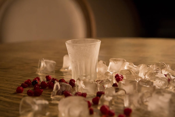 Крижаний спиртний постріл з льодом і ягодами на дерев'яному столі
 - Фото, зображення