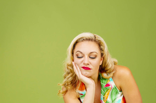 Portrait of a grumpy blonde woman looking down, isolated on green studio background - Photo, Image