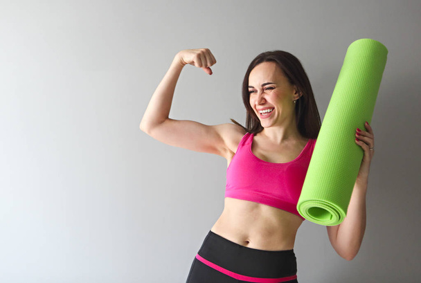Atraktivní žena nosí růžové sportovní drží zelené jógu nebo fitness mat po cvičit doma nebo v klubu. Příjemný usměvavý sportovní instruktor s yogamatce - Fotografie, Obrázek