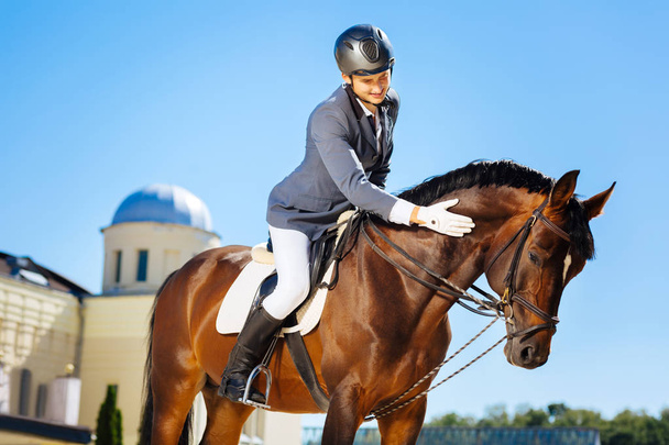 Handsome smiling man wearing helmet petting horse - Foto, Imagen