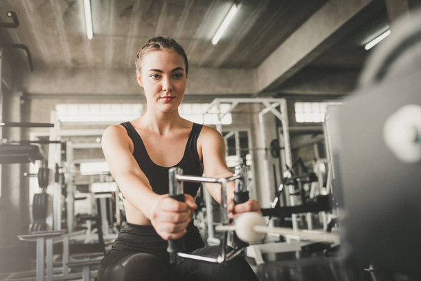 Hermosa joven saludable mujer caucásica haciendo ejercicio con la máquina de traning por cable en el gimnasio
 - Foto, imagen