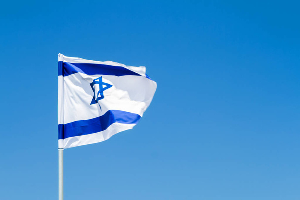 Flag of in the wind, National flag of Israel with Star of David against the blue sky - Fotó, kép