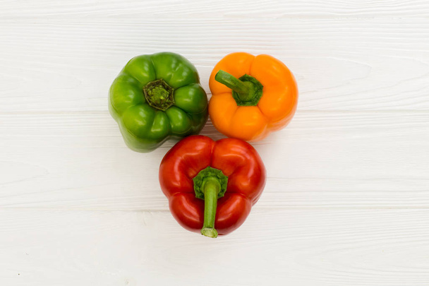 Three different color bulgarian pepper on the wooden board on the white ooden table. - Фото, зображення