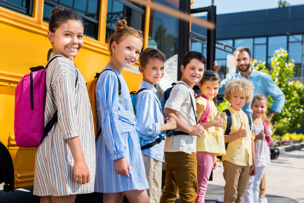очередь счастливых учеников, стоящих возле школьного автобуса с учителем
 - Фото, изображение