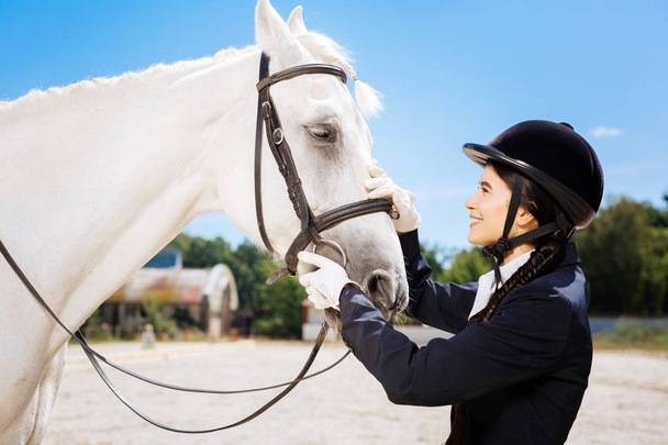 Young promising horsewoman coming to her lovely white horse - Foto, imagen