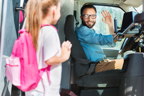 усміхнений водій автобуса вітає школярку, яка входить в автобус
 - Фото, зображення