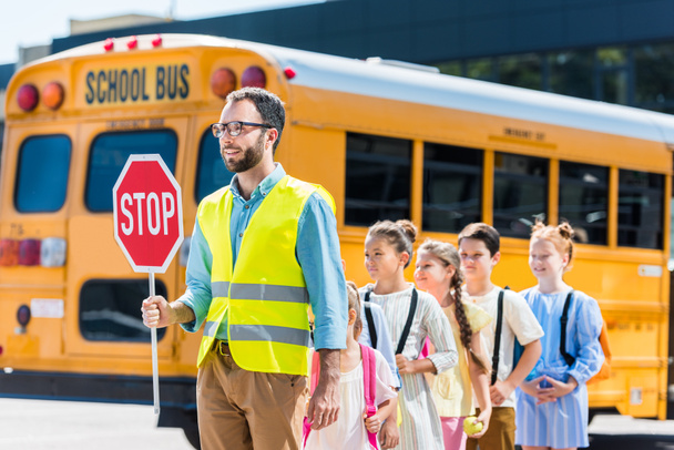 охоронець перетинає дорогу зі школярами перед шкільним автобусом
 - Фото, зображення
