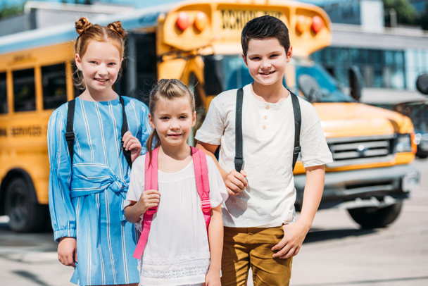 group of smiling pupils looking at camera in front of school bus - Valokuva, kuva