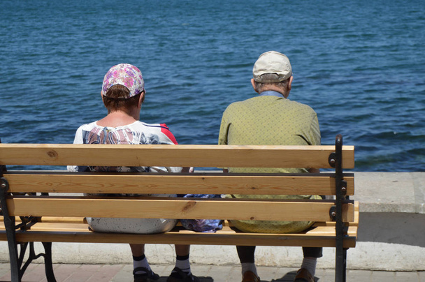 Пожилая пара смотрит на море, сидя на скамейке. Концепция отдыха и путешествия пенсионеров
 - Фото, изображение