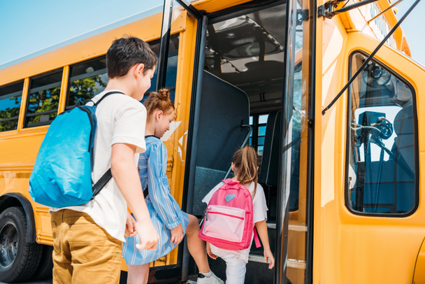 вид сзади учеников с рюкзаками, въезжающих в школьный автобус
 - Фото, изображение