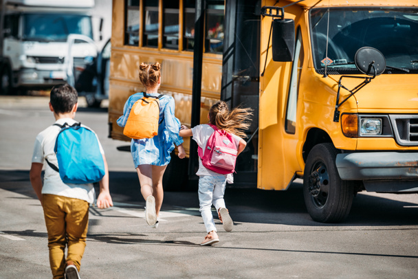 вид сзади на группу школьников, бегущих в школьный автобус
 - Фото, изображение