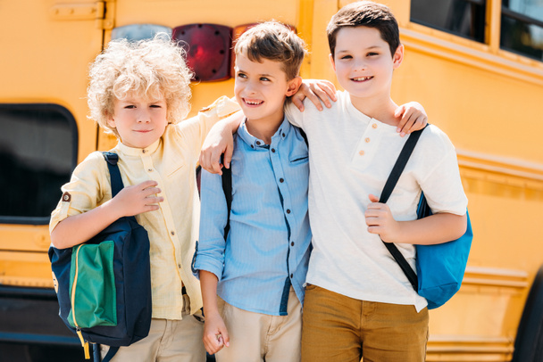 entzückende kleine Schüler, die sich vor dem Schulbus umarmen  - Foto, Bild