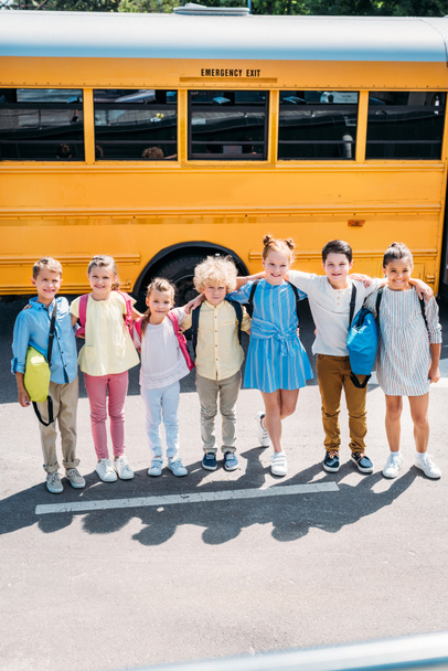 groupe d'écoliers heureux debout devant le bus scolaire et regardant la caméra
 - Photo, image