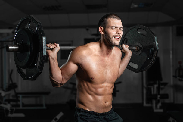 Handsome weightlifter lifting barbells with Squats. Male training with barbell, pumping legs - 写真・画像