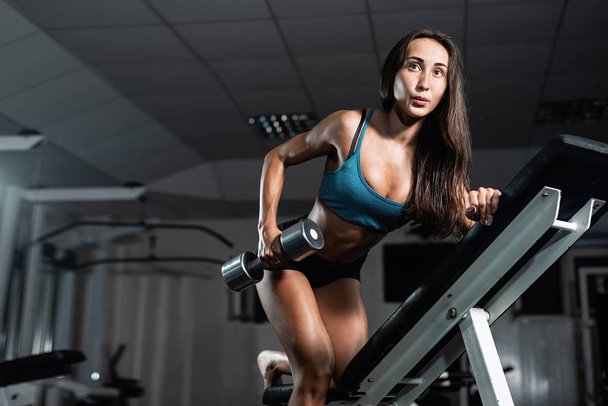 A woman trains in the gym. Athletic woman trains with dumbbells, pumping her biceps - Foto, Imagem