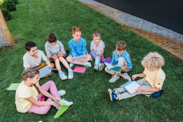 высокий угол обзора группы учащихся, сидящих на траве с книгами и устройствами
 - Фото, изображение