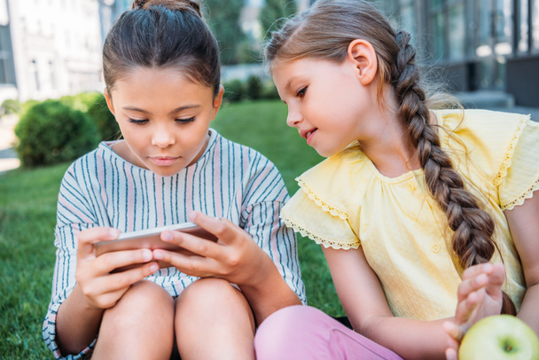 adorable little schoolgirls using smartphone together - Foto, afbeelding