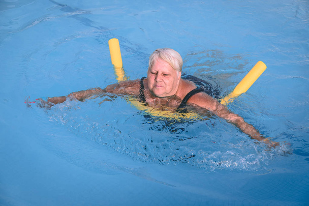 Una mujer mayor se aferra a un dispositivo de flotación en una piscina para aprender a nadar
 - Foto, imagen
