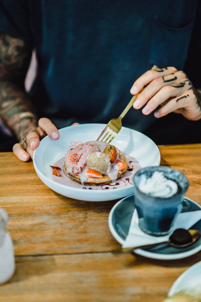 Young tattooed man eating pancakes. hands, smartphone and food.  - Foto, Bild