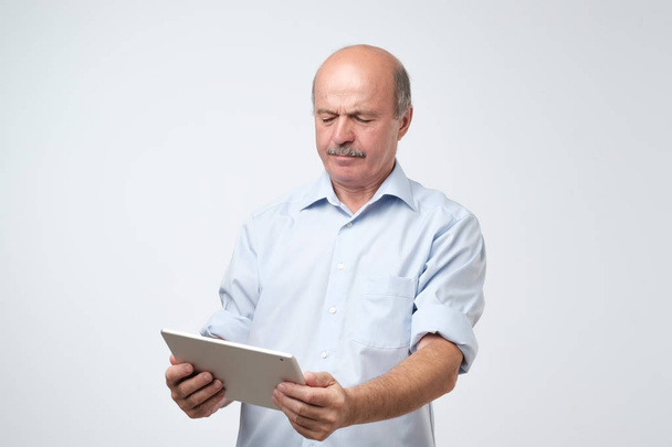Ώριμος άνδρας Ευρωπαϊκό χρησιμοποιώντας ένα ψηφιακό tablet. Είναι αμηχανία και σύγχυση. Δεν ήξερε πώς να χρησιμοποιήσετε το νέο gadget του - Φωτογραφία, εικόνα