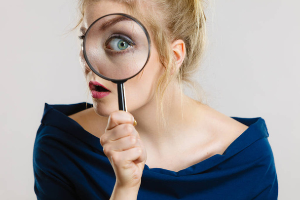 Blonde woman holding magnifying glass investigating something and looking closely, trying to find solution. - Photo, Image