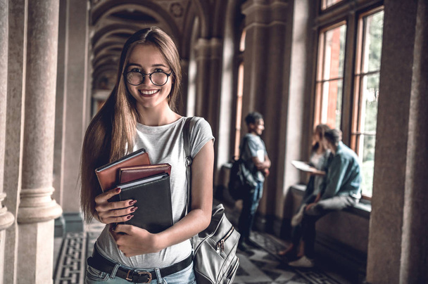 College life.Beautiful student in glasses holding books and looking at camera. - Фото, изображение