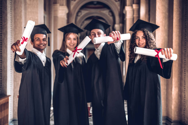 We worked hard and got results!Group of smiling graduates showing their diplomas ,standing together in university hall and looking at camera. - Zdjęcie, obraz