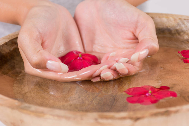 Young girl hand in wooden bowl with water and red flower, natural manicure on finger nails. Spa treatment for hands concept. Close up, selective focus - Photo, image