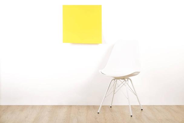 Single empty loft style chair on wooden floor with blank ad poster and white wall background, yellow sticker with copy space for your text. Interview invitation for vacant position concept. Close up. - Zdjęcie, obraz