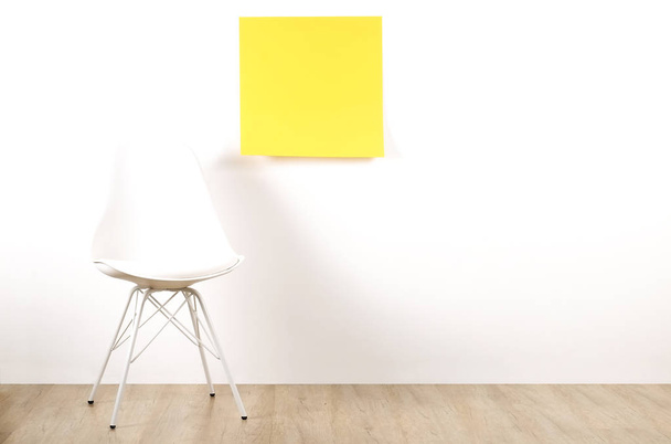 einzelner leerer Loft-Stuhl auf Holzboden mit leerem Werbeposter und weißem Wandhintergrund, gelber Aufkleber mit Kopierplatz für Ihren Text. Einladung zum Vorstellungsgespräch zum Stellenkonzept. Nahaufnahme. - Foto, Bild