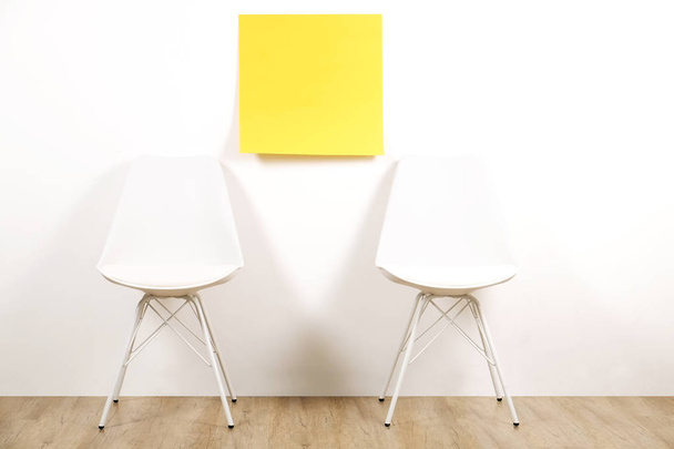 Pair of seats, two empty loft style chairs on wooden floor with blank ad poster & white wall background, yellow sticker, copy space for text. Interview invitation for vacant position concept. Close up - Foto, afbeelding