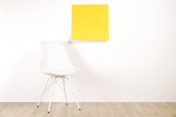 Single empty loft style chair on wooden floor with blank ad poster and white wall background, yellow sticker with copy space for your text. Interview invitation for vacant position concept. Close up. - Foto, Imagem