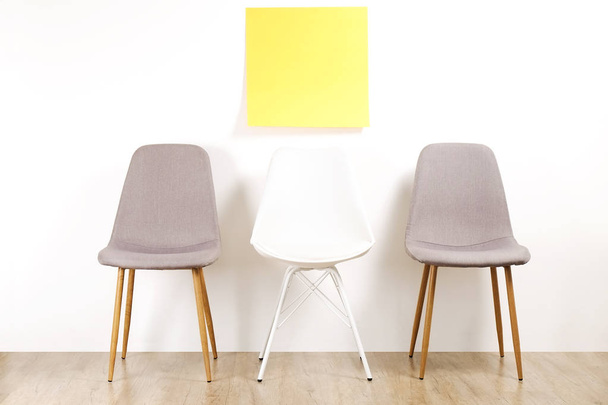 Three empty available loft style chair seats on wooden floor with blank ad poster, white wall background, yellow copy space sticker for text. Interview invitation for vacant position concept. Close up - 写真・画像