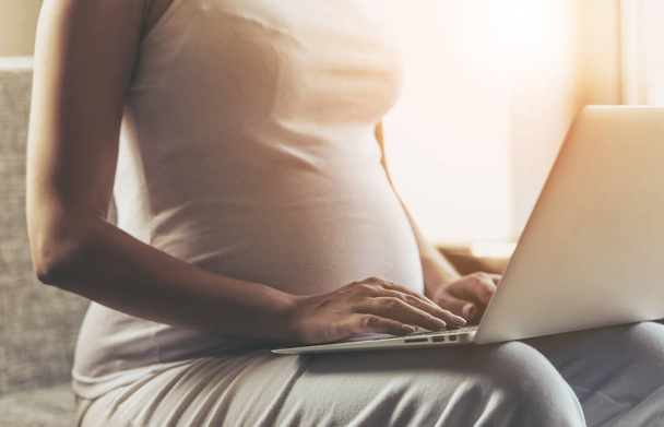 Pregnant Woman Using Laptop and Sitting on Sofa. - 写真・画像
