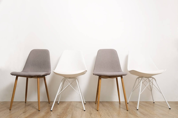 Multiple white gray elegant loft style empty chairs standing in room, wooden floor & big blank wall background with a lot of copy space for text. Vacant seats. Human resources hiring campaign concept - Foto, Imagem