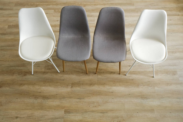 Group therapy counseling for addicts & alcoholics concept. Multiple loft style empty chairs, white & gray, standing in row on wood textured floor. Four available seats. Copy space background, close up - Foto, Imagen